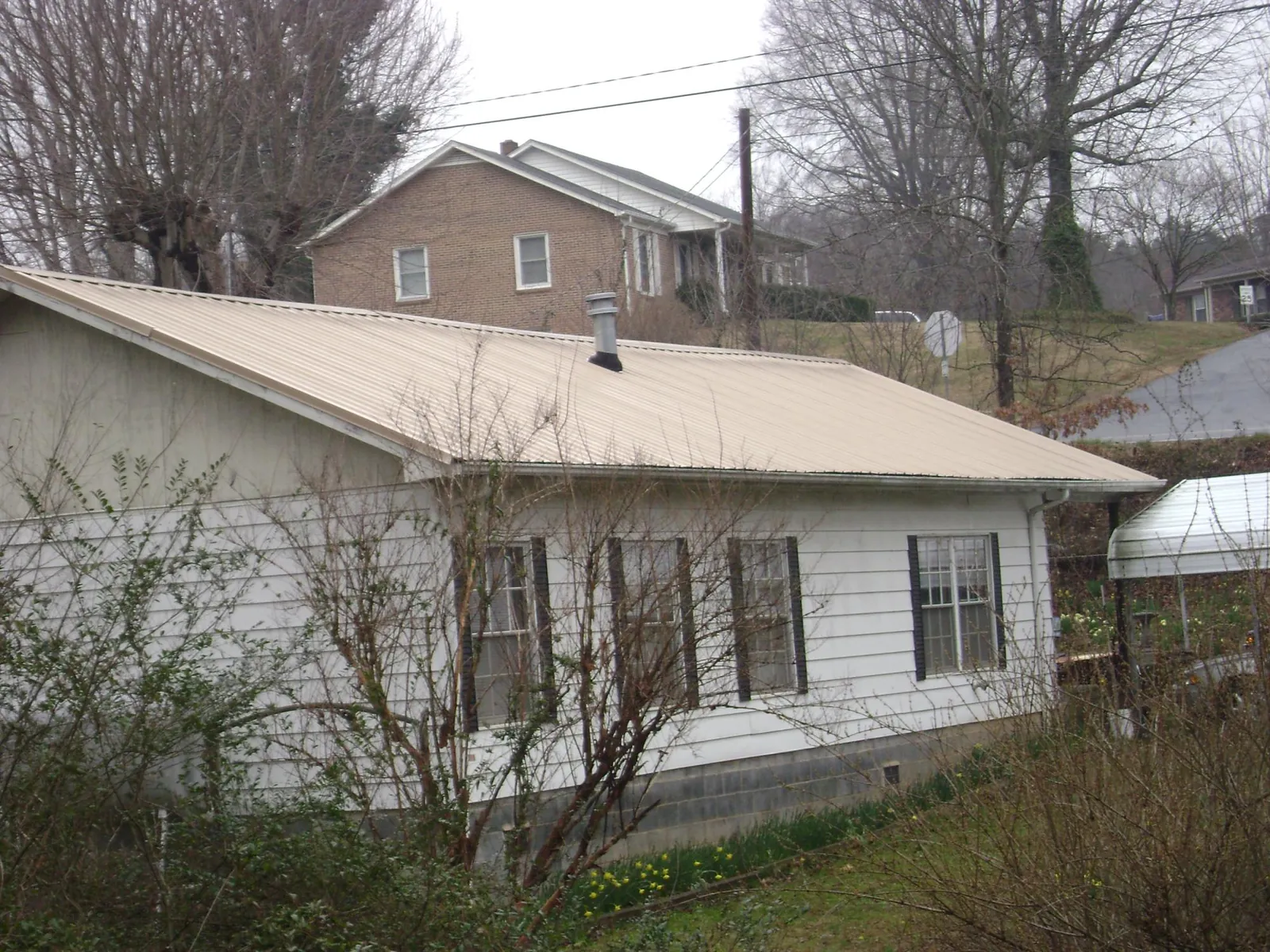 Tan metal roof on a white sided house set into a hillside — Commercial Roofing by Roofing Brothers in Rose Hill