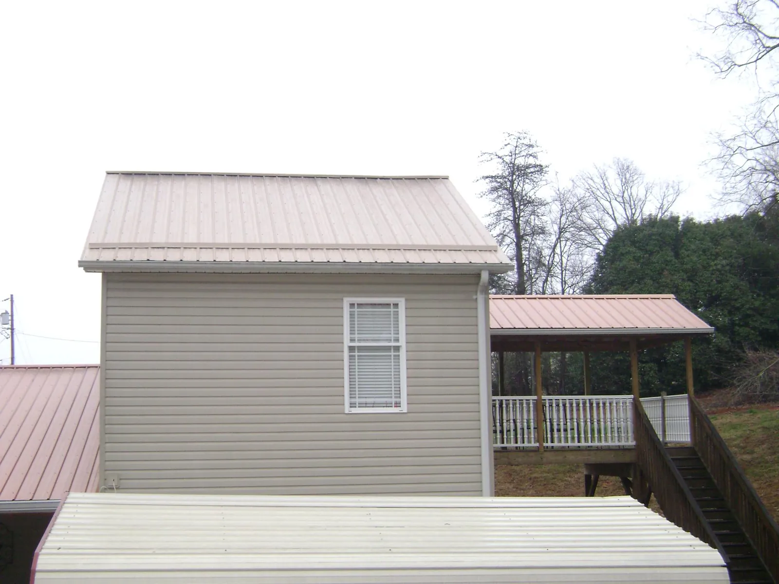 Tan metal roofs on a two story addition and attached porch, from a Roof Replacement job in Rose Hill